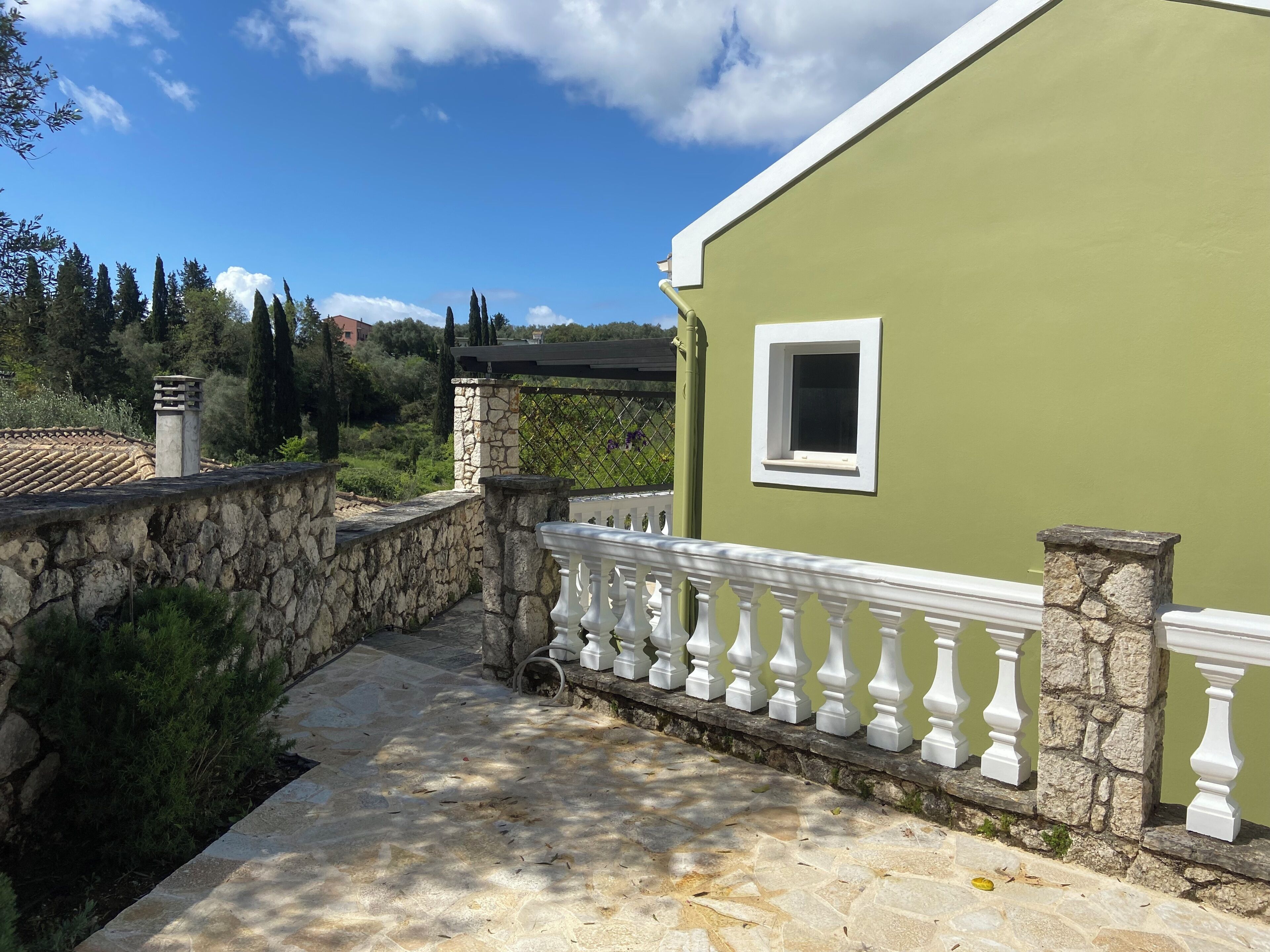 A stone wall, a white balustrade, and a green building with a window.