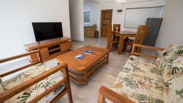 Una sala de estar con televisor, muebles de madera, un sofá estampado con motivos tropicales y un comedor.