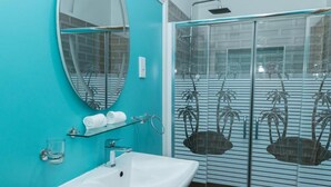 Een badkamer met een witte wastafel, een spiegel en een douchecabine van glas met palmboommotieven.