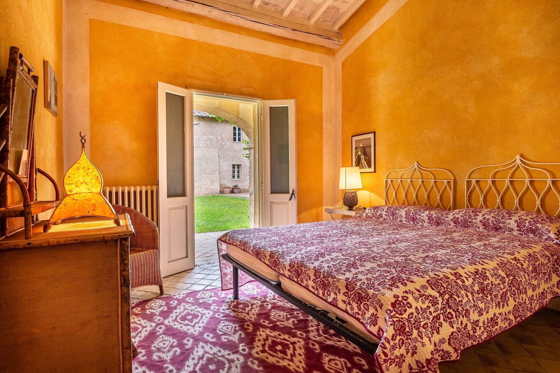 A bedroom with a bed, a nightstand, a lamp, and a view of the outside.