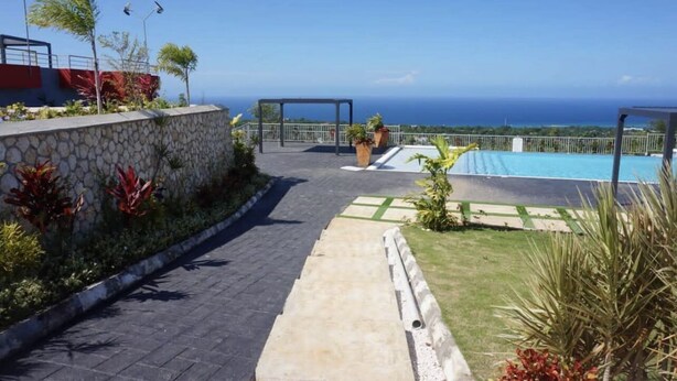 A pathway leading to a pool with a view of the ocean, surrounded by plants and a stone wall. - Chic Hideaway a Paradise Home in Jamaica (Ocho Rios)