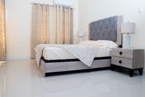 A modern bedroom with a bed, bedside table, lamp, and patterned curtains.