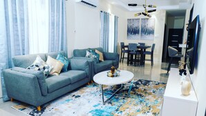A modern living room with a grey sofa, a round coffee table, and a dining area with a table and chairs. - Chic Hideaway a Paradise Home in Jamaica (Ocho Rios)