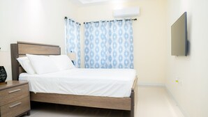 A bedroom with a bed, nightstand, and wall-mounted TV. - Chic Hideaway a Paradise Home in Jamaica (Ocho Rios)