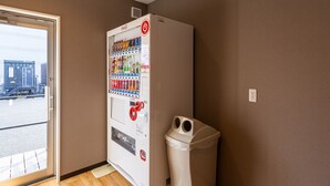 Ein Getränkeautomat mit Coca-Cola-Logo, ein Mülleimer und ein Fenster mit Blick auf ein Gebäude.