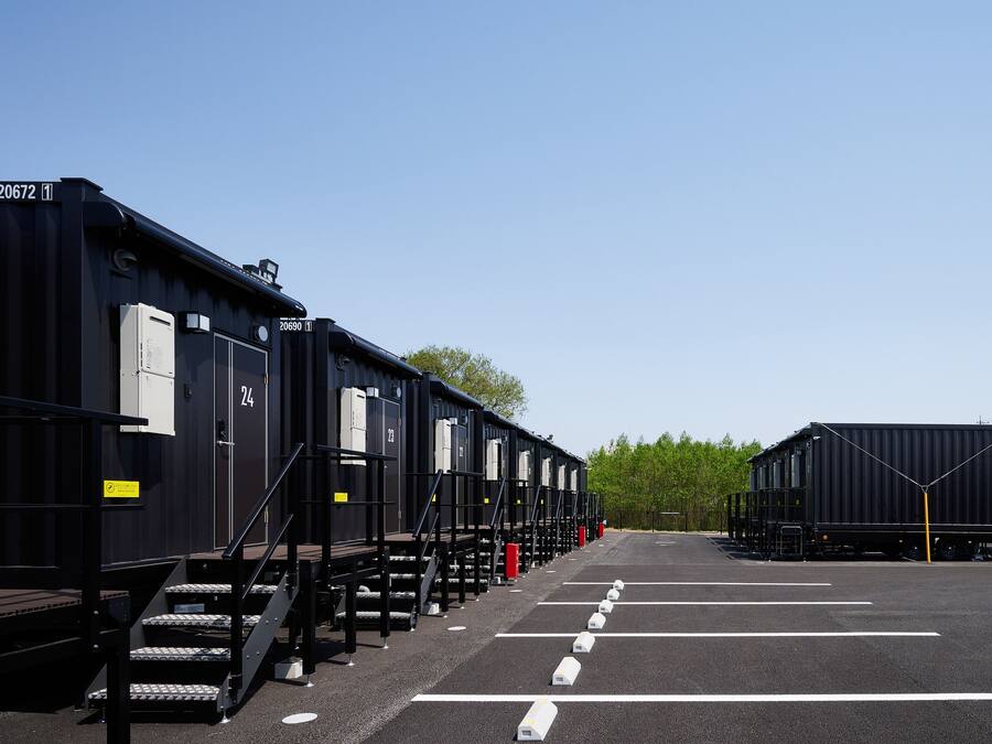 En rad svarta tågvagnar med numrerade dörrar, en parkeringsplats med vita linjer och en klarblå himmel.