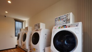 Ein Waschraum mit vier Frontlader-Waschmaschinen, die an einer Wand mit einem Fenster aufgereiht sind.