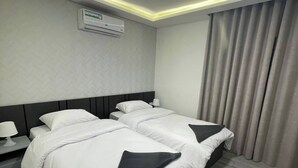 Ein Hotelzimmer mit zwei Betten, einem Nachttisch mit Lampe, einer Klimaanlage und einem Fenster mit Vorhängen.