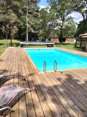 Une terrasse en bois avec une piscine, un escalier métallique pour la piscine et un espace abrité.