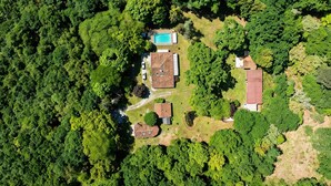 Vista aérea de una propiedad con piscina, varias edificaciones y abundante vegetación circundante.