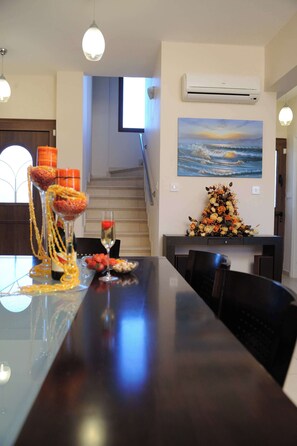 A dining area with a long table, decorative flowers, and a painting of a sunset on the wall. - Three Bedroom Villa With Private Pool and Landscaped Garden Close to the Beach (Pissouri)