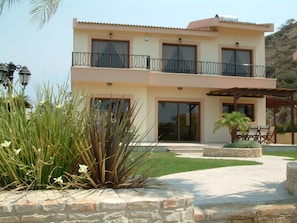 A two-story building with a balcony, stone walls, and a patio area with outdoor furniture. - Three Bedroom Villa With Private Pool and Landscaped Garden Close to the Beach (Pissouri)