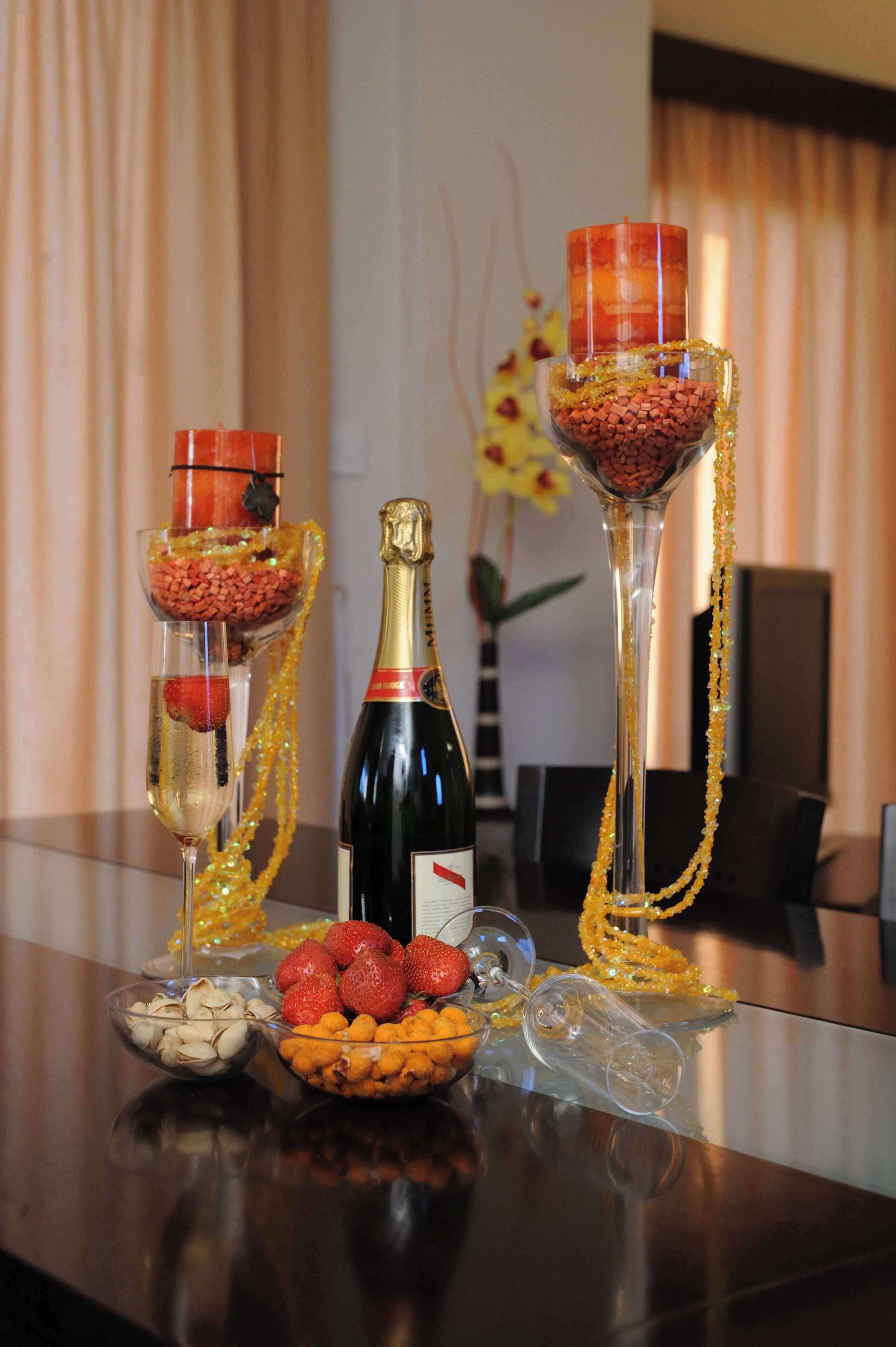 Una mesa con una botella de champán, dos copas con frutas y cuentas, y un bol de nueces.