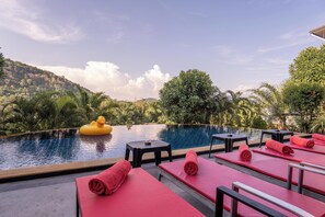 Un espace aménagé au bord de la piscine, avec des chaises longues, une plateforme flottante et une vue sur un paysage montagneux.