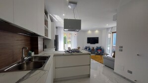 A modern kitchen with a central island, stainless steel sink, and a built-in oven. - Vanesia's Luxury Suits (Sanremo)