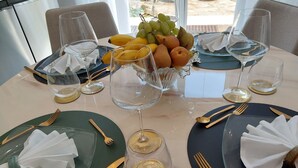 A dining table set with plates, cutlery, and wine glasses, with a fruit bowl in the center. - Vanesia's Luxury Suits (Sanremo)