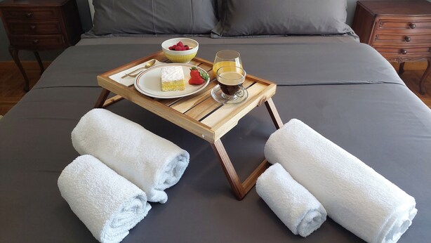 A neatly made bed with grey bedding, a tray with breakfast items, and two bedside tables with lamps. - Vanesia's Luxury Suits (Sanremo)