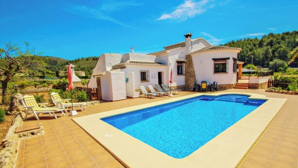 A poolside area with a rectangular pool, lounge chairs, and a white building with a tiled roof. - Quicano - magnificent views and private pool in Lliber (Lliber)