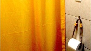 Une salle de bain avec un rideau de douche jaune, un porte-serviettes avec une serviette et un porte-rouleau de papier toilette fixé au mur.