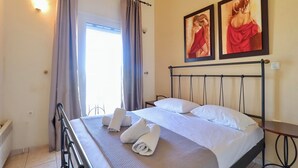 Quarto de hotel com cama, duas pinturas, janela com cortinas e radiador.