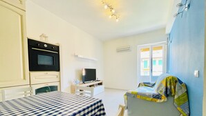 Una habitación pequeña con cama, televisión, kitchenette y ventana.