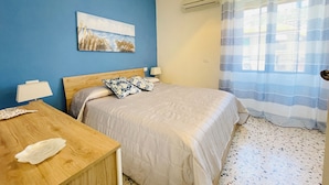 Un dormitorio con cama, mesita de noche, lámpara, un cuadro en la pared y un equipo de aire acondicionado.