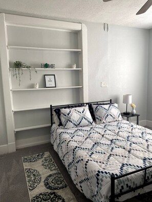 Cozy retreat with a patterned quilt, a shelving unit, and a bedside table.