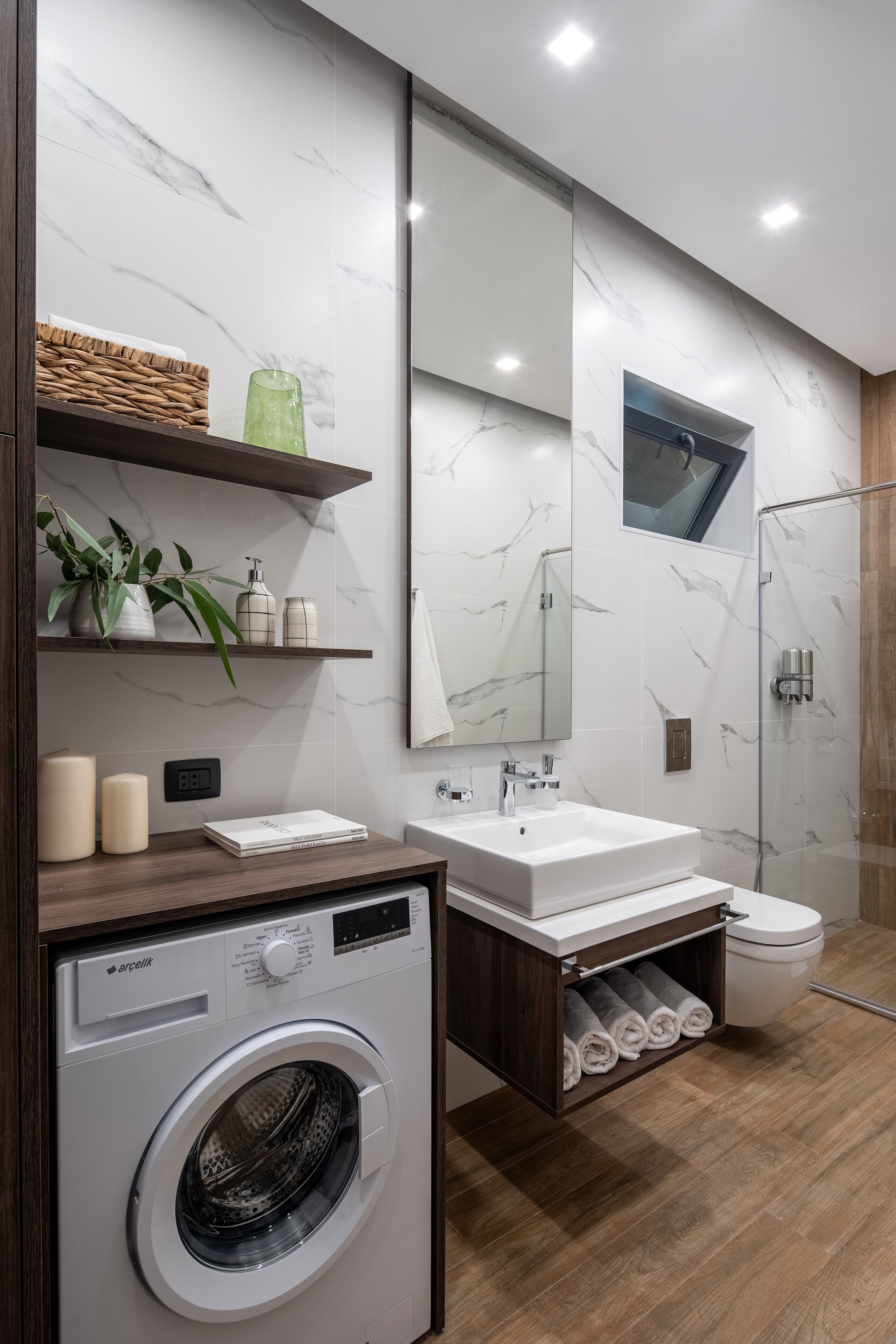 A modern bathroom with a marble wall, a large mirror, a washing machine, a sink, and a toilet.