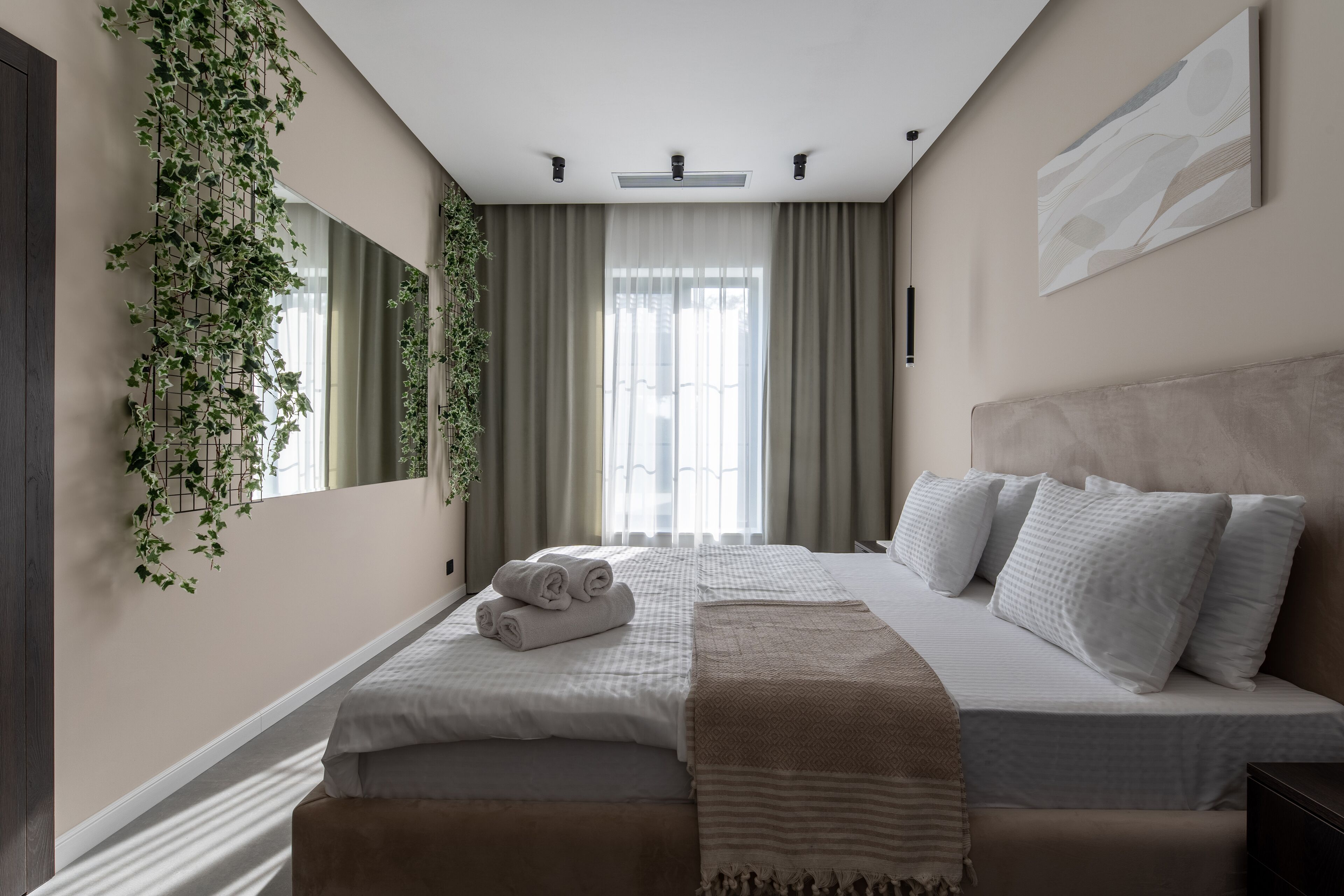 A bedroom with a large bed, a bedside table, a mirror, and a window with curtains.