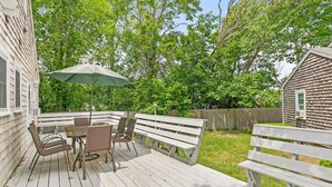 Une terrasse en bois aménagée avec du mobilier d’extérieur, notamment une table, des chaises et un banc.