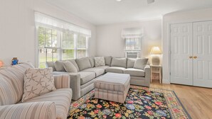 Un salon avec un canapé d’angle, un pouf et un tapis à motifs floraux.
