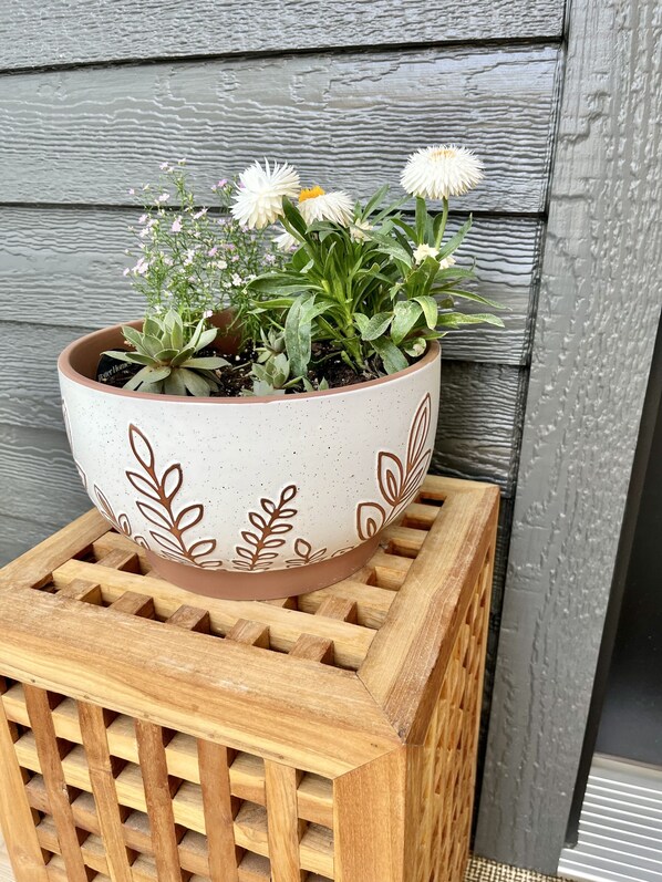 Een bloempot met witte bloemen en groene bladeren op een houten standaard.