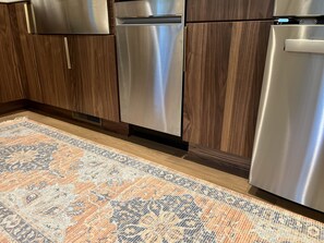 Kitchen features stainless steel appliances, a refrigerator, and a dishwasher, complemented by warm cabinetry and a patterned rug.