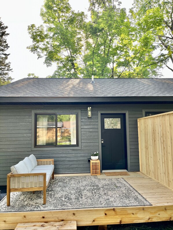 Step into this charming home, featuring a cozy seating area with a bench and chair on a wooden deck surrounded by lush greenery.
