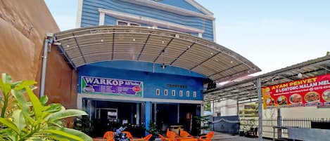 Un edificio con fachada azul y una zona de acceso cubierta con sillas de plástico naranja.