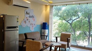 A modern room with a ceiling fan, a refrigerator, seating area with chairs and a table, a wall map, and a large window with a view of trees.