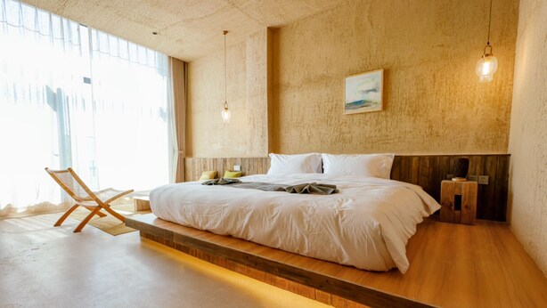 A modern bedroom with a large bed, wooden platform, and a chair. - Steppe Valley Resort (Xing'an)