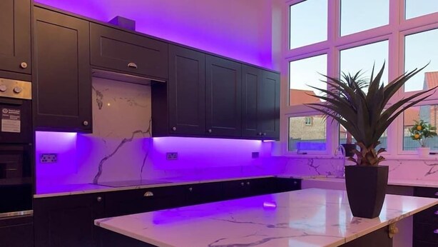 A modern kitchen with dark cabinets, a marble countertop, and purple ambient lighting. - Bodham House & Halls - 9 bedrooms (Bodham)