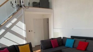 Una sala de estar moderna con un sofá modular, una mesa de centro de madera y una escalera que sube a un nivel superior.