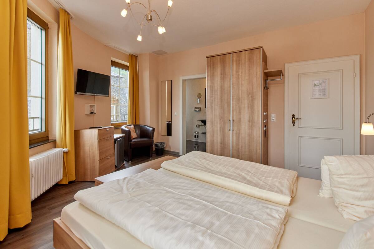 A hotel room with two beds, a desk, a chair, a TV, and a wardrobe.