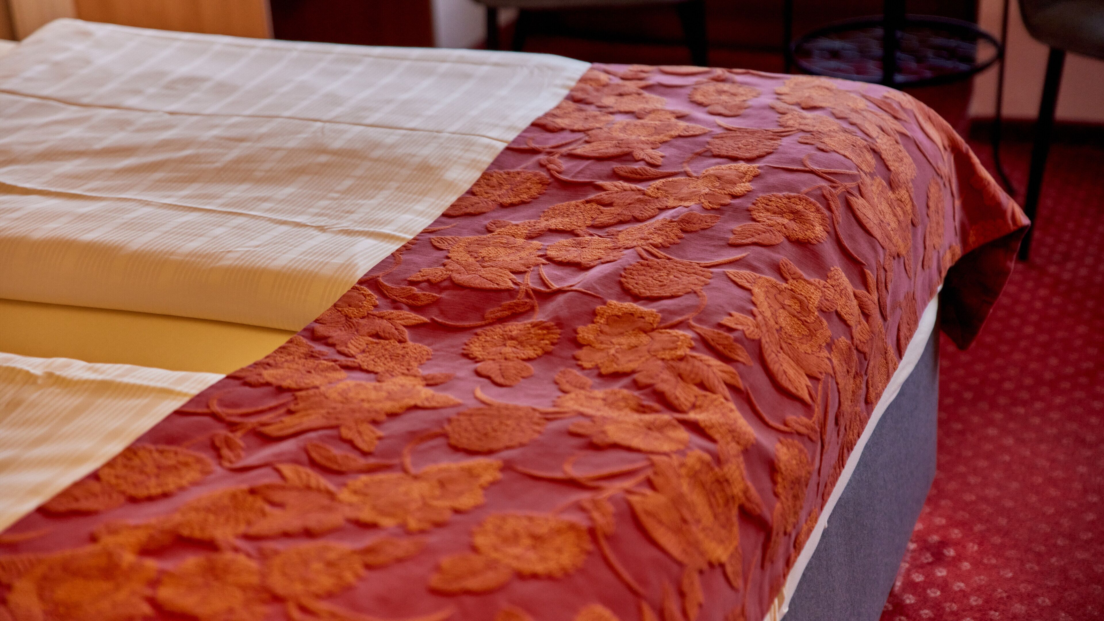 A bed with a patterned bedspread and a plain white sheet.