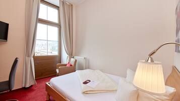 A hotel room with a bed, a desk, a chair, a lamp, and a window with curtains.