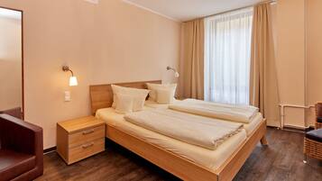 A modern hotel room with a wooden bed, bedside lamps, a nightstand, a chair, and a large window with curtains.