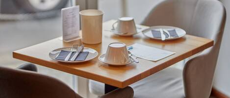 Een nette, moderne eetruimte met een houten tafel gedekt voor twee personen, inclusief borden, bestek en een kopje.