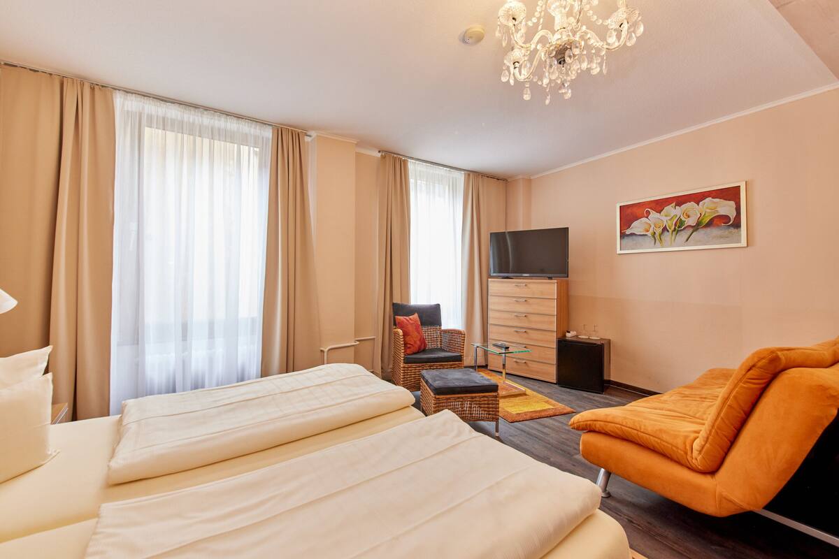 A hotel room with a large bed, a TV, a painting, and a chandelier.