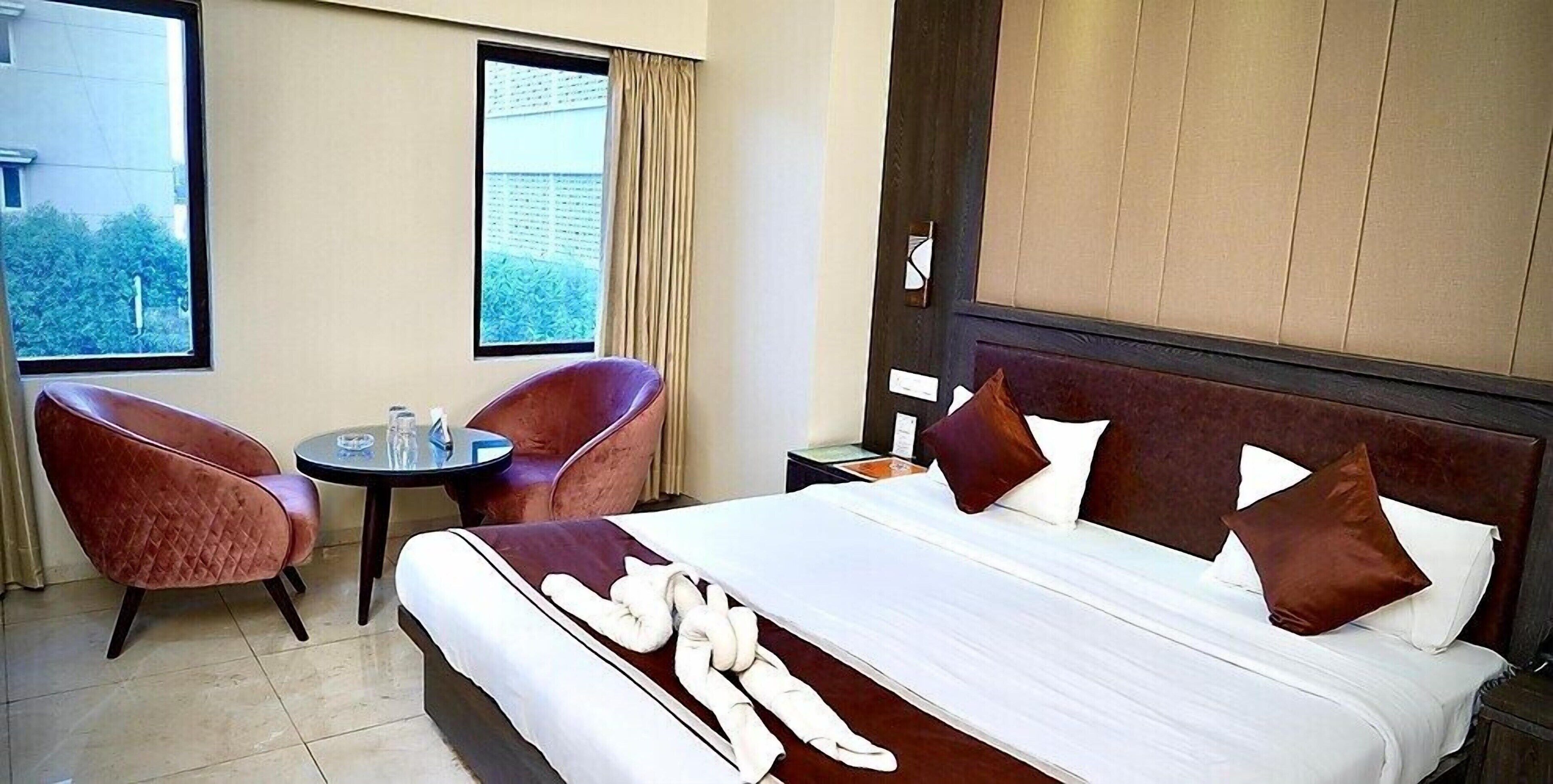 A hotel room with a bed, two armchairs, a small table, and a window with curtains.