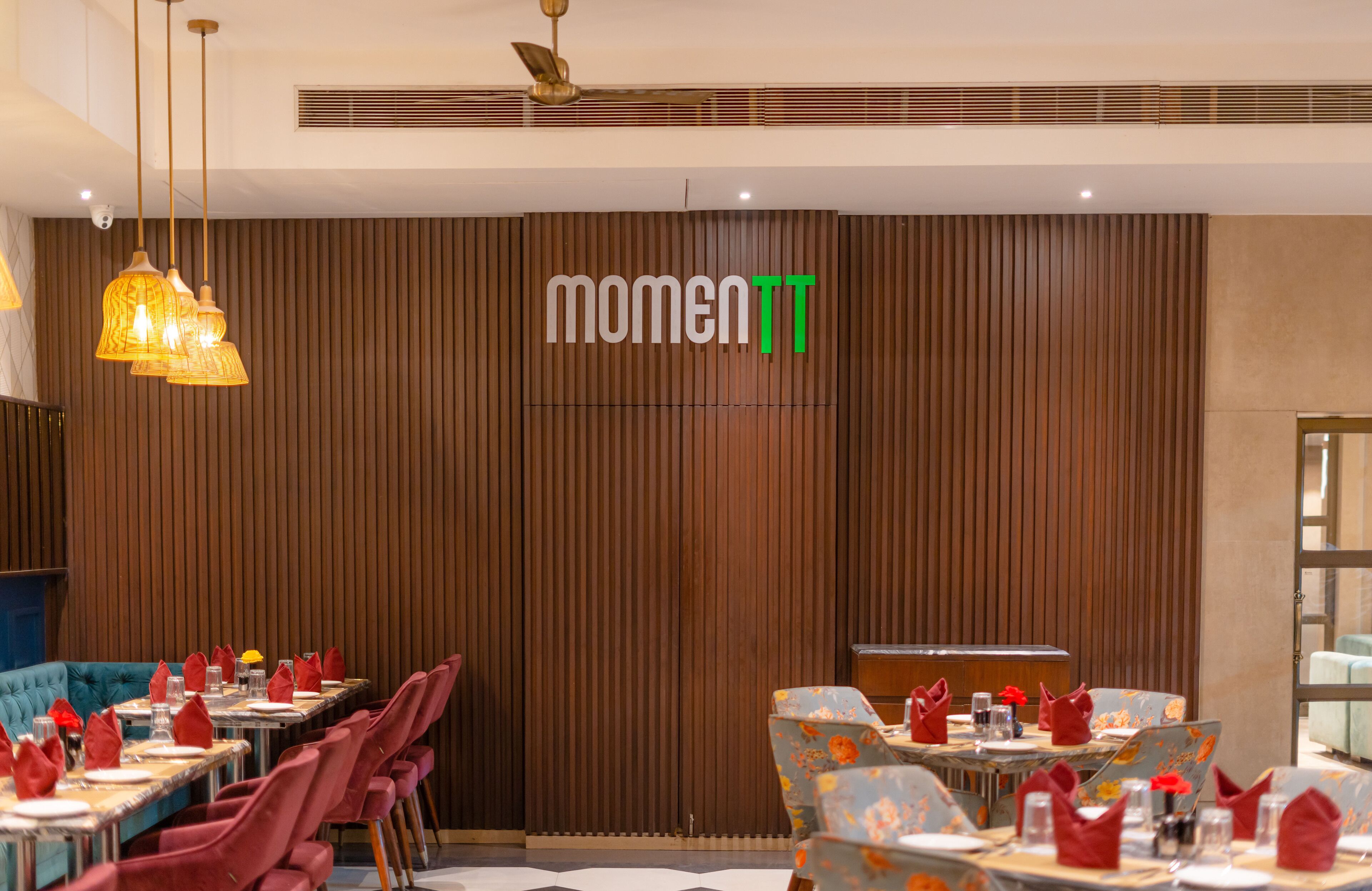 A restaurant with wooden panel walls, tables set with red napkins, and hanging pendant lights.