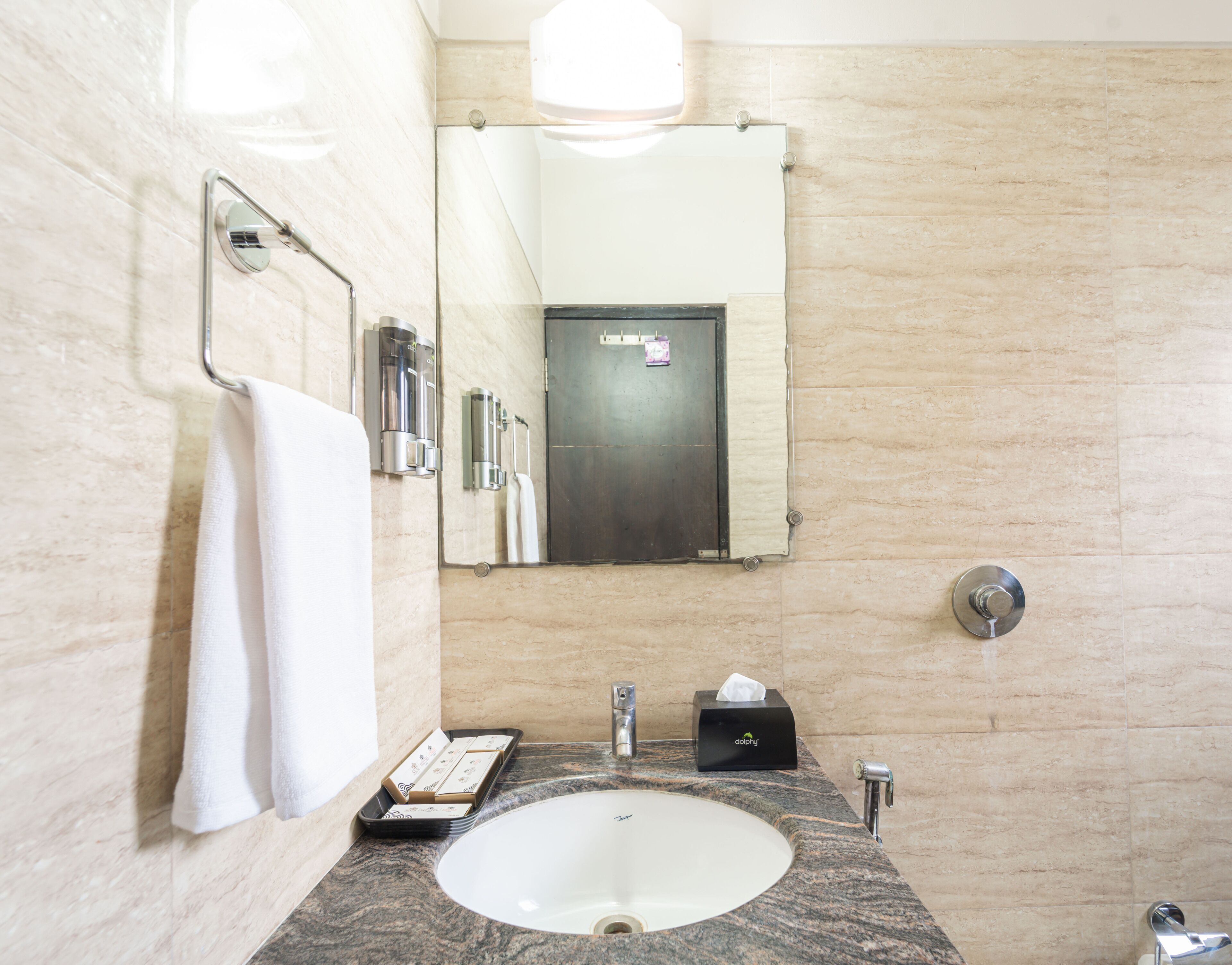 Une salle de bain équipée d’un lavabo en marbre, d’un porte-serviettes, d’un miroir, d’un distributeur de savon et d’un porte-rouleau de papier toilette.