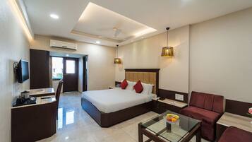 A hotel room with a bed, a desk, a chair, a glass table, and a sofa.