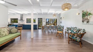 Ampla sala de estar com mesa de jantar, cadeiras, um sofá e cozinha ao fundo.